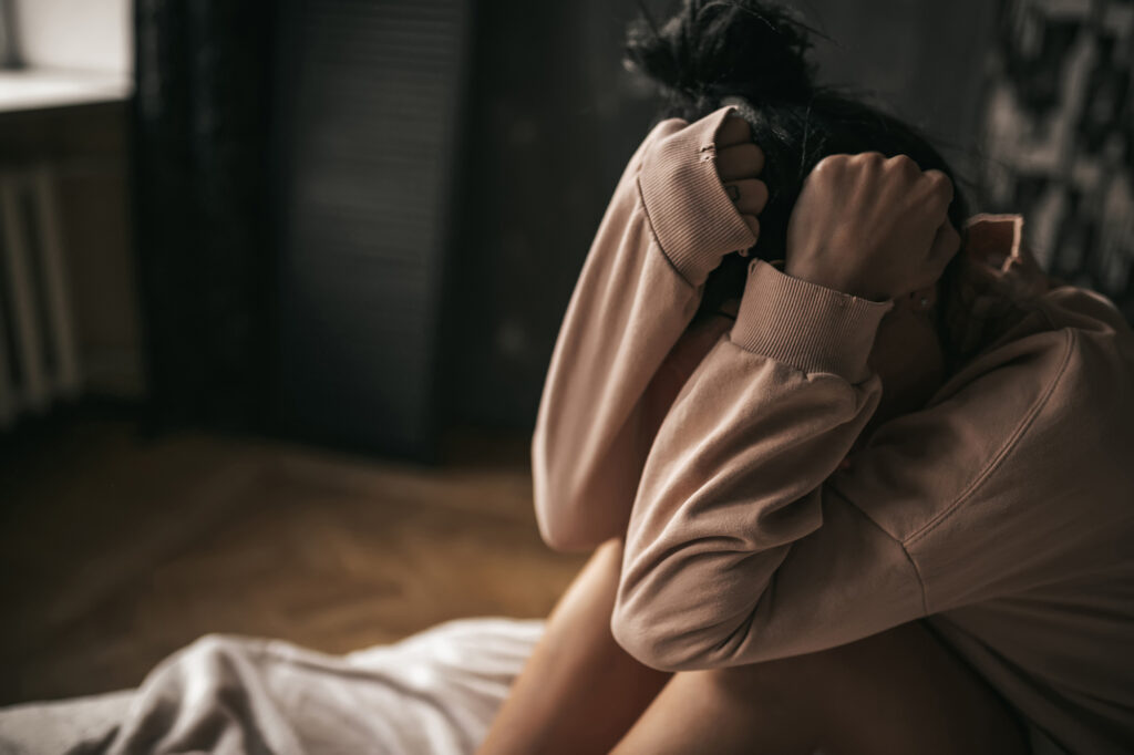 Kobieta siedzi na łóżku w stanie depresyjnym, chowając głowę w ramionach.